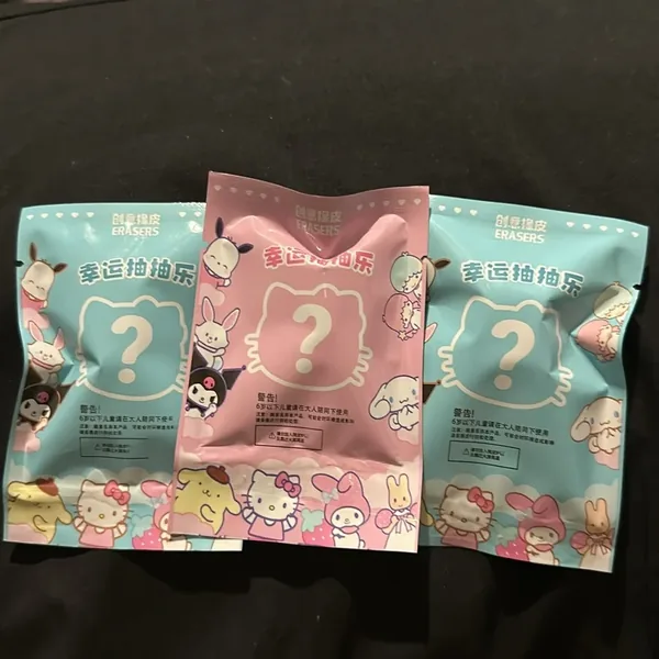 The backs of three packs: a big question mark inside a cat-head outline, so you can’t see which eraser is inside