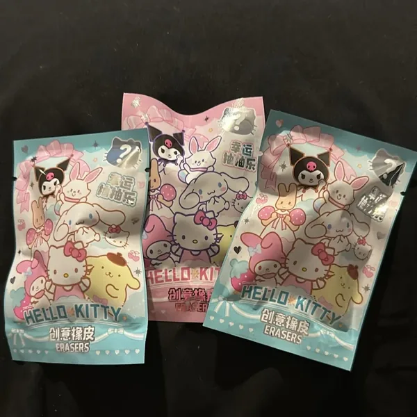 Three sealed packs, one pink and two blue, printed with Hello Kitty, Kuromi, My Melody, Cinnamoroll and Pompompurin